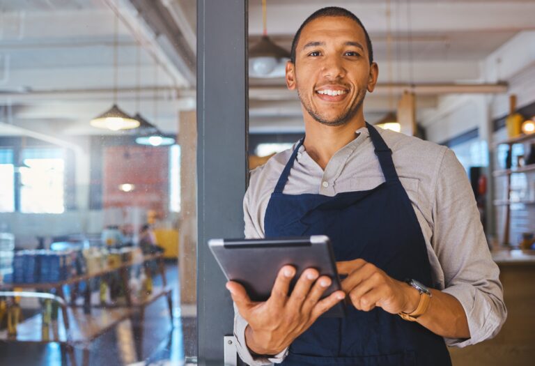 Smiling restaurant manager leaning against a pillar and working on a tablet