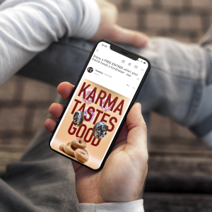 A person sitting and holding a smartphone, the screen shows a fundraiser advertisement and reads "Karma Tastes Good".